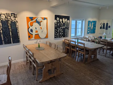 A wider view of the bright Ryvarden dining and gallery hall, with several large striking canvases lining the white walls above long rustic wooden tables