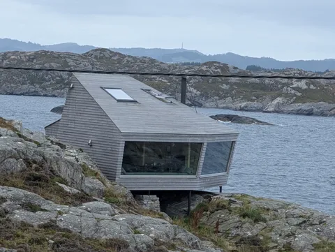 One of the Floke cottages at Ryvarden — an angular timber cabin with a panoramic window, perched on the rocky shoreline above the sea