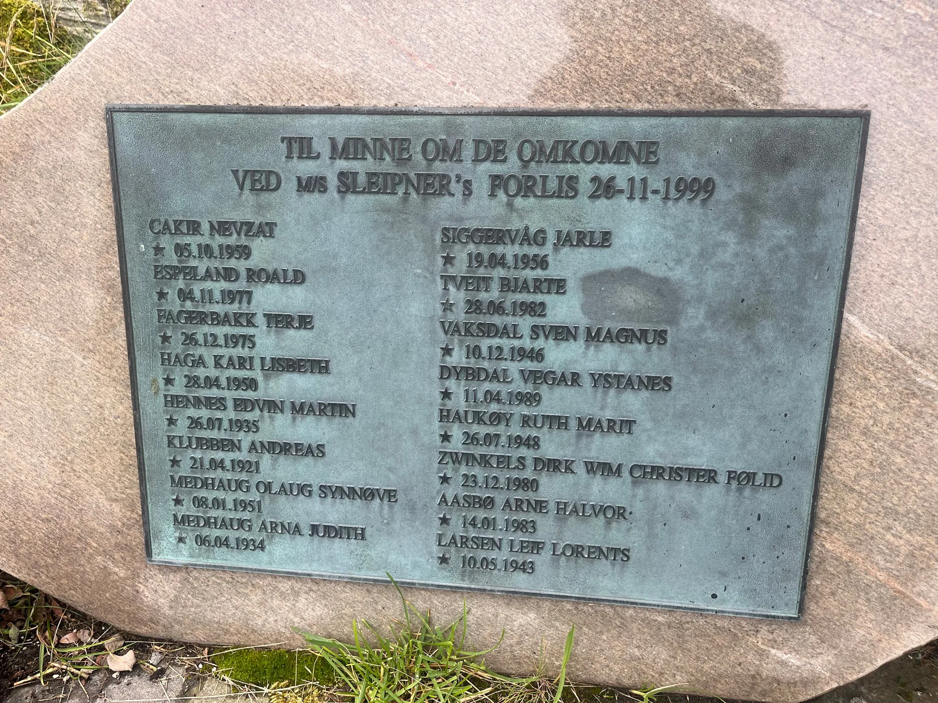 The weathered green bronze memorial plaque reading 'Til minne om de omkomne ved M/S Sleipner's forlis 26-11-1999', listing the names and birth dates of the sixteen people who lost their lives