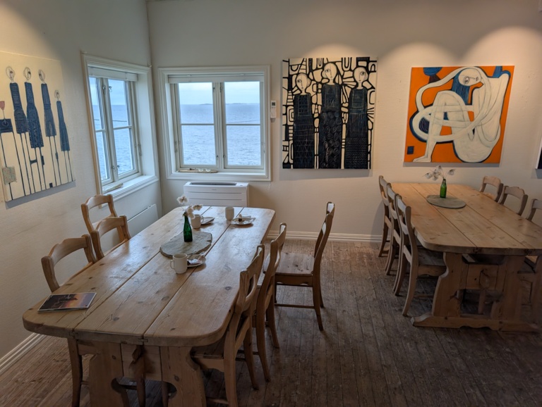 The Ryvarden cafeteria dining room with rustic wooden tables, bold modern paintings on the walls and corner windows opening onto the sea
