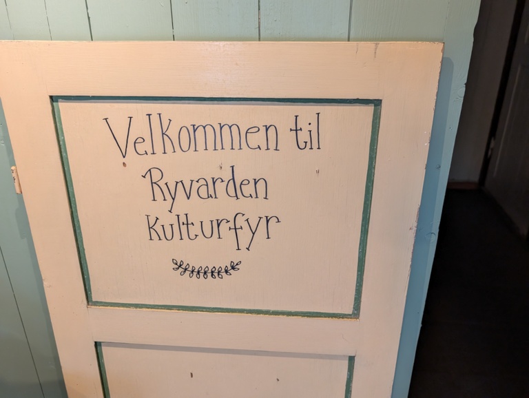 A hand-painted cream and green door with dark blue script reading 'Velkommen til Ryvarden Kulturfyr'