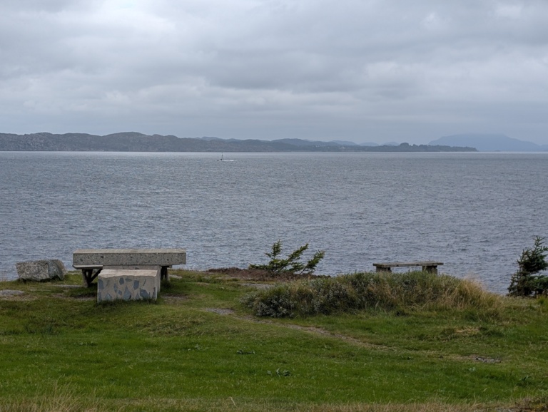 A grassy viewpoint with benches and a picnic table looking out over the sea along the walk